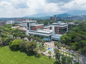 A modern building with a flat roof and a mix of glass and brick facades, surrounded by greenery and a clear sky.