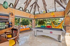 A pool table labeled 'ENGLAND' with a British flag, surrounded by a brick wall and wooden beams, with a hammock and outdoor seating area visible.
