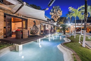 A pool area with a hanging chair, a covered seating area, and a building with a brick facade.
