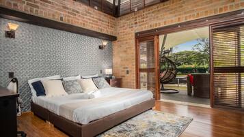 A bedroom with a large bed, a wooden floor, a patterned wall, and a view through a glass door.