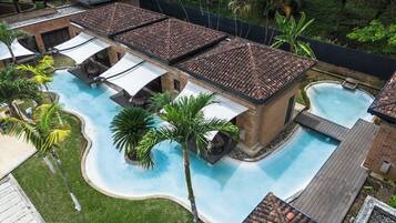 A swimming pool with a tiled roof, surrounded by palm trees and a brick building.
