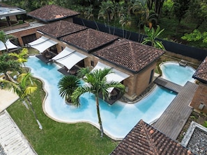 A swimming pool with a tiled roof, surrounded by palm trees and a brick building.