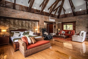 A spacious room with a large bed, a seating area with a red sofa and white armchair, and a brick wall.