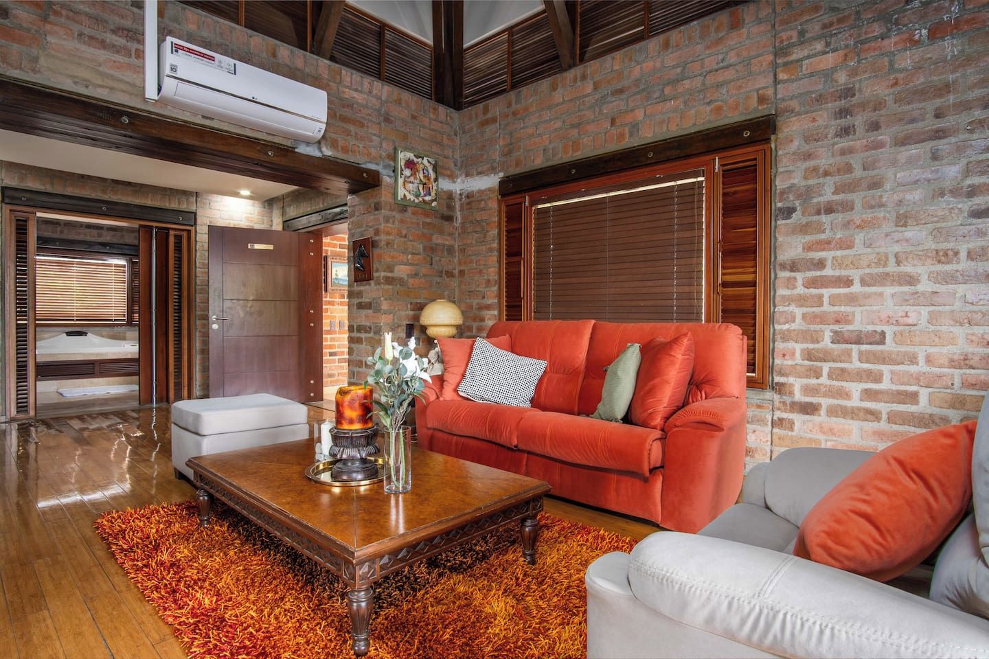A living room with a brick wall, a red sofa, a white armchair, a wooden coffee table, and a fireplace.