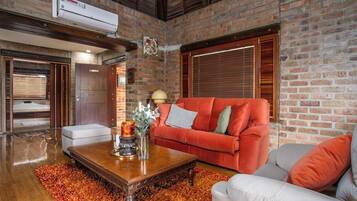 A living room with a brick wall, a red sofa, a white armchair, a wooden coffee table, and a fireplace.