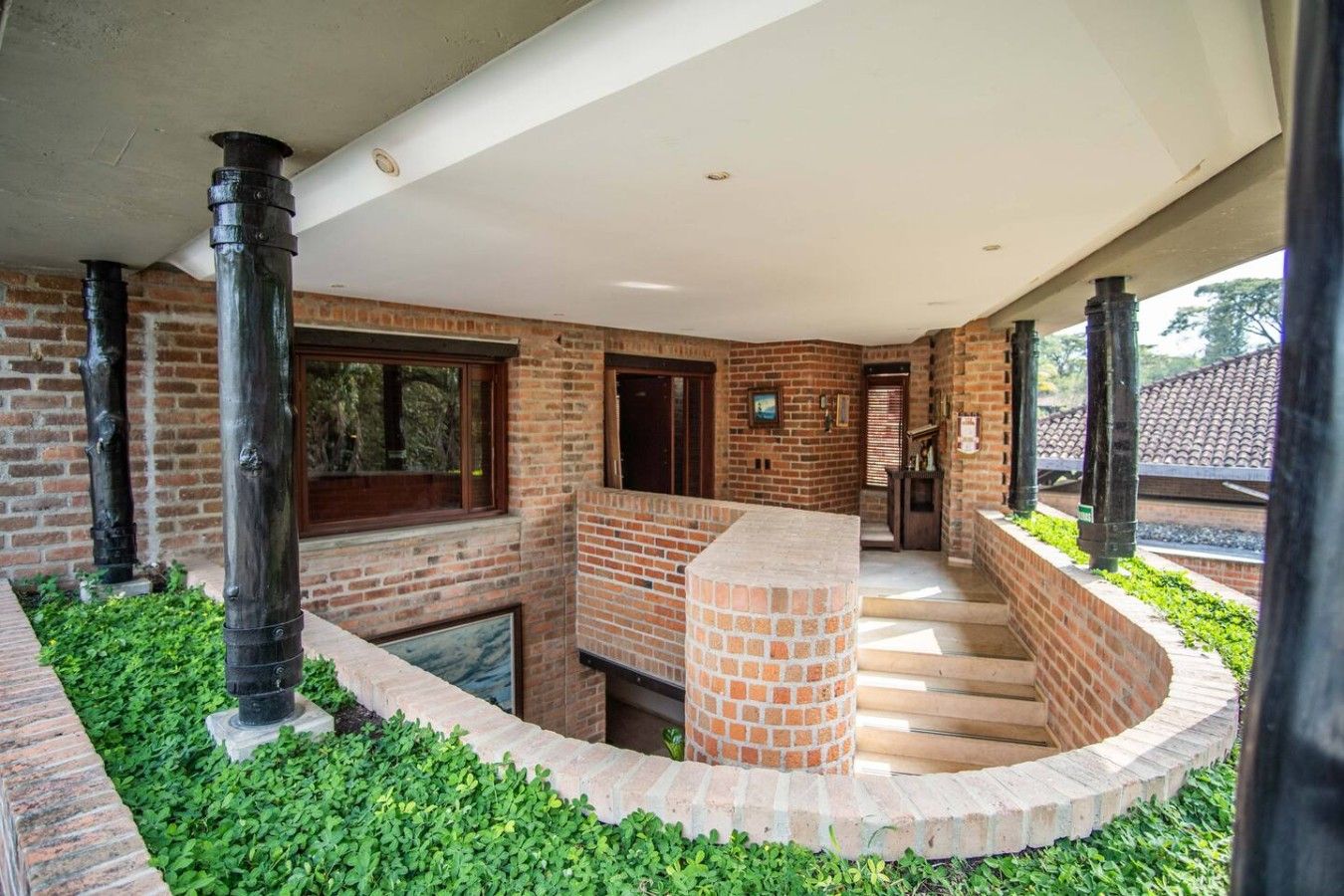 A covered outdoor area with brick walls, a central brick column, and a staircase leading to an upper level.