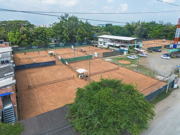 A tennis court with a net, surrounded by a fence, and adjacent to a building with a flat roof.