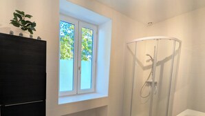 Et moderne badeværelse med glasbrusekabine, indbygget vindue og et mørkt træskab.
