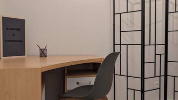 Een kamer met een houten bureau, een zwarte mesh-stoel, een lijst met een bordje aan de muur en een zwart tussenscherm.