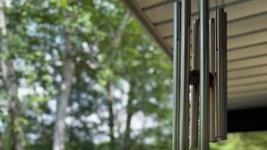 A wind chime hanging from a ceiling, a round wooden object below it, and a view of a lake with trees in the background. - Lodge No Complaints - Harrison (Harrison)