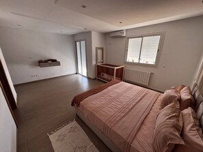 Ein Schlafzimmer mit einem großen Bett, einem Holckrippenbett, einem Heizkörper und einem Fenster mit Jalousien.