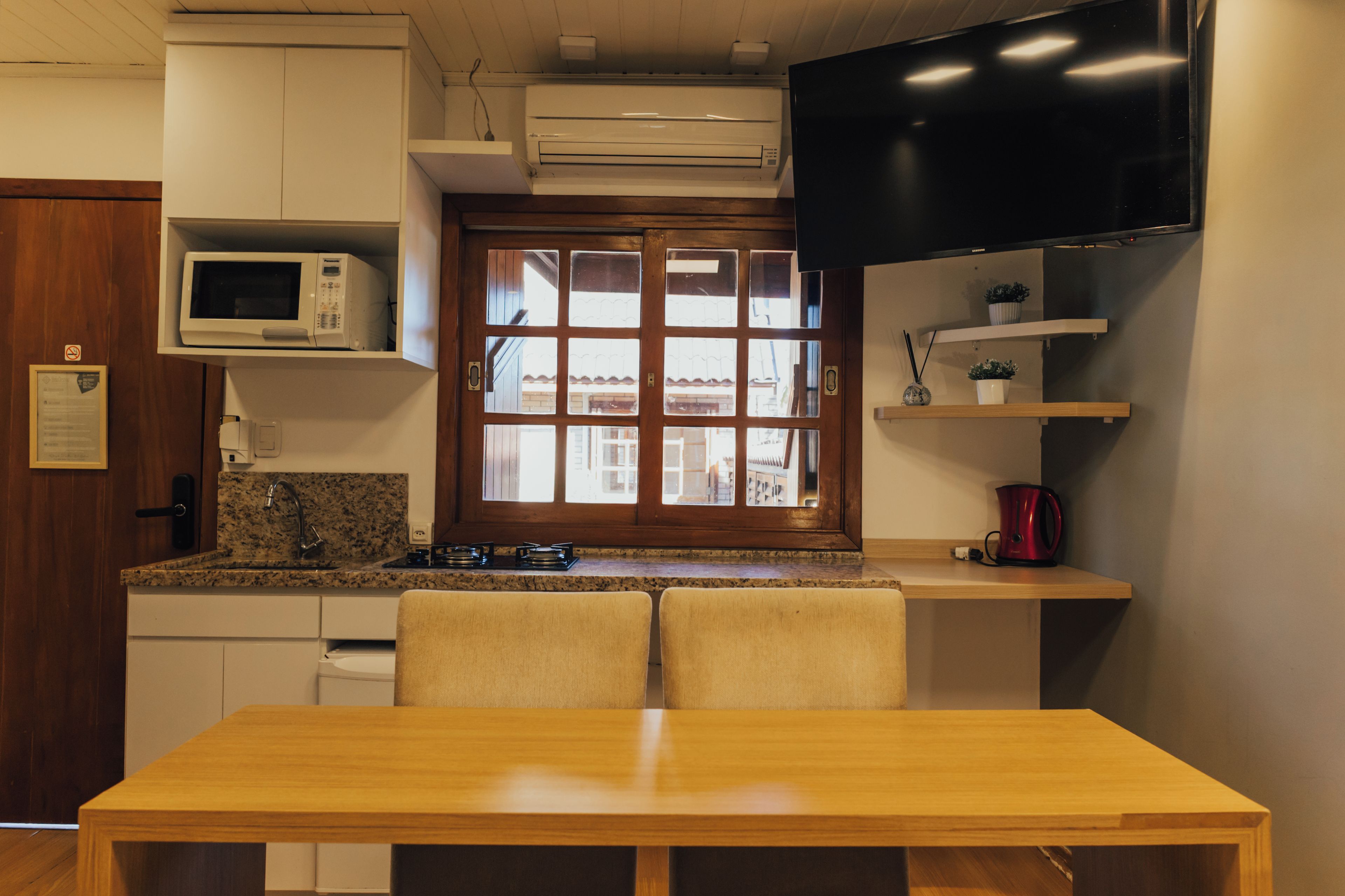 A compact kitchen with a dining table, microwave, stove, and a TV mounted above the counter.