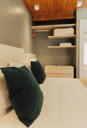 Un dormitorio con cama, almohadas, mesita de noche y estanterías empotradas.