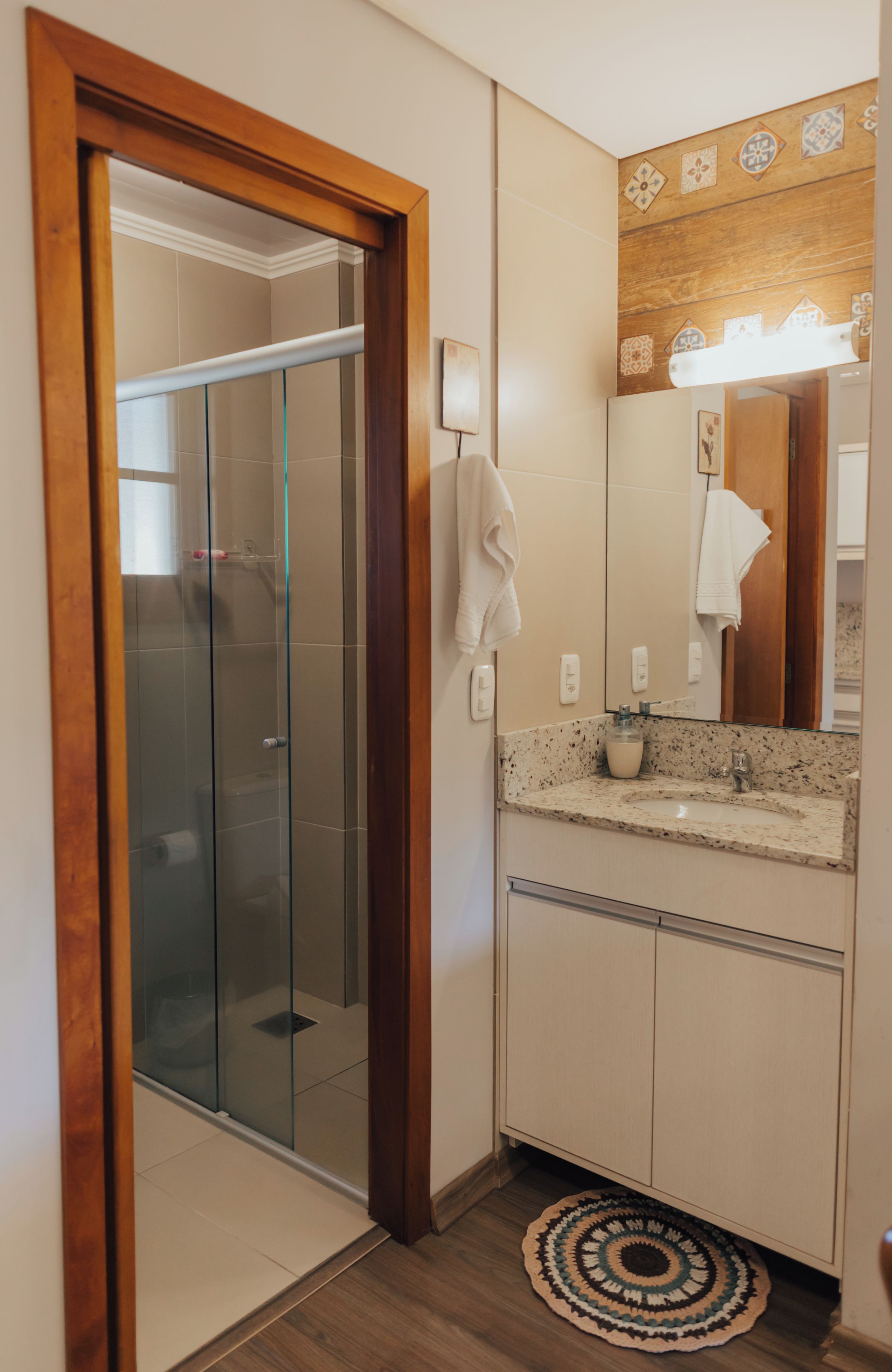 A bathroom with a glass shower enclosure, a sink with a soap dispenser, and a towel hanging on the wall.