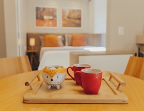 Una mesa de madera con una bandeja que sostiene una taza de cerámica con forma de búho y dos tazas rojas.