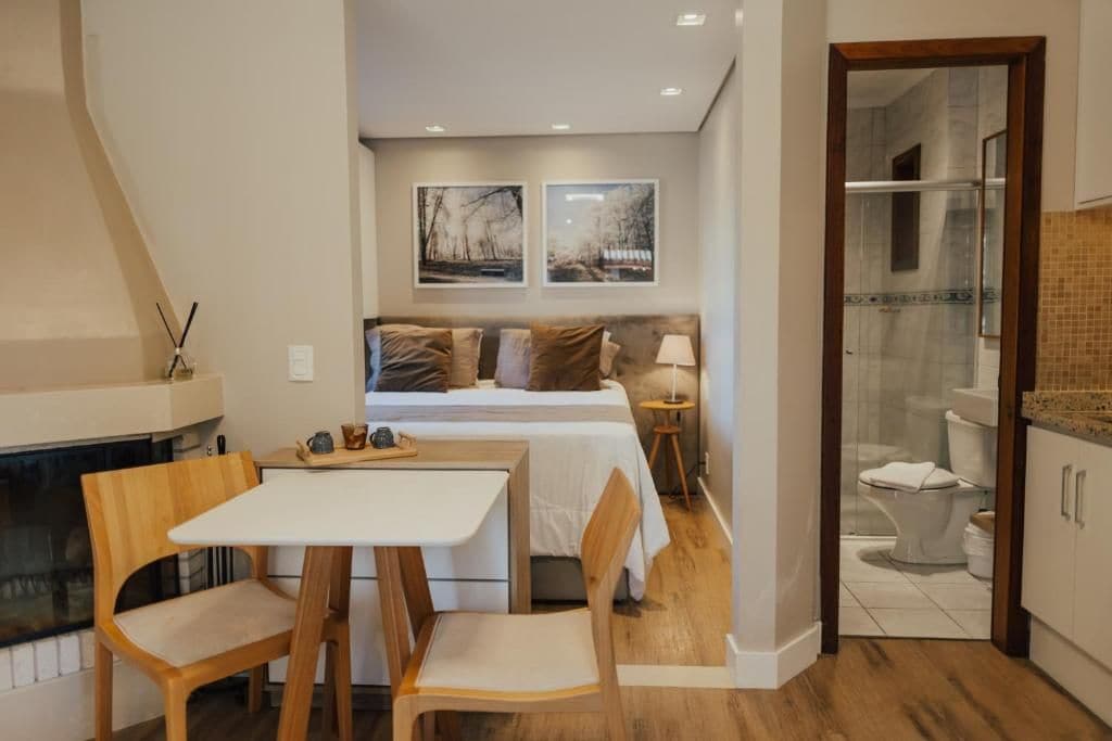 A bedroom with a bed, bedside tables, a nightstand, a fireplace, and a view into the bathroom.