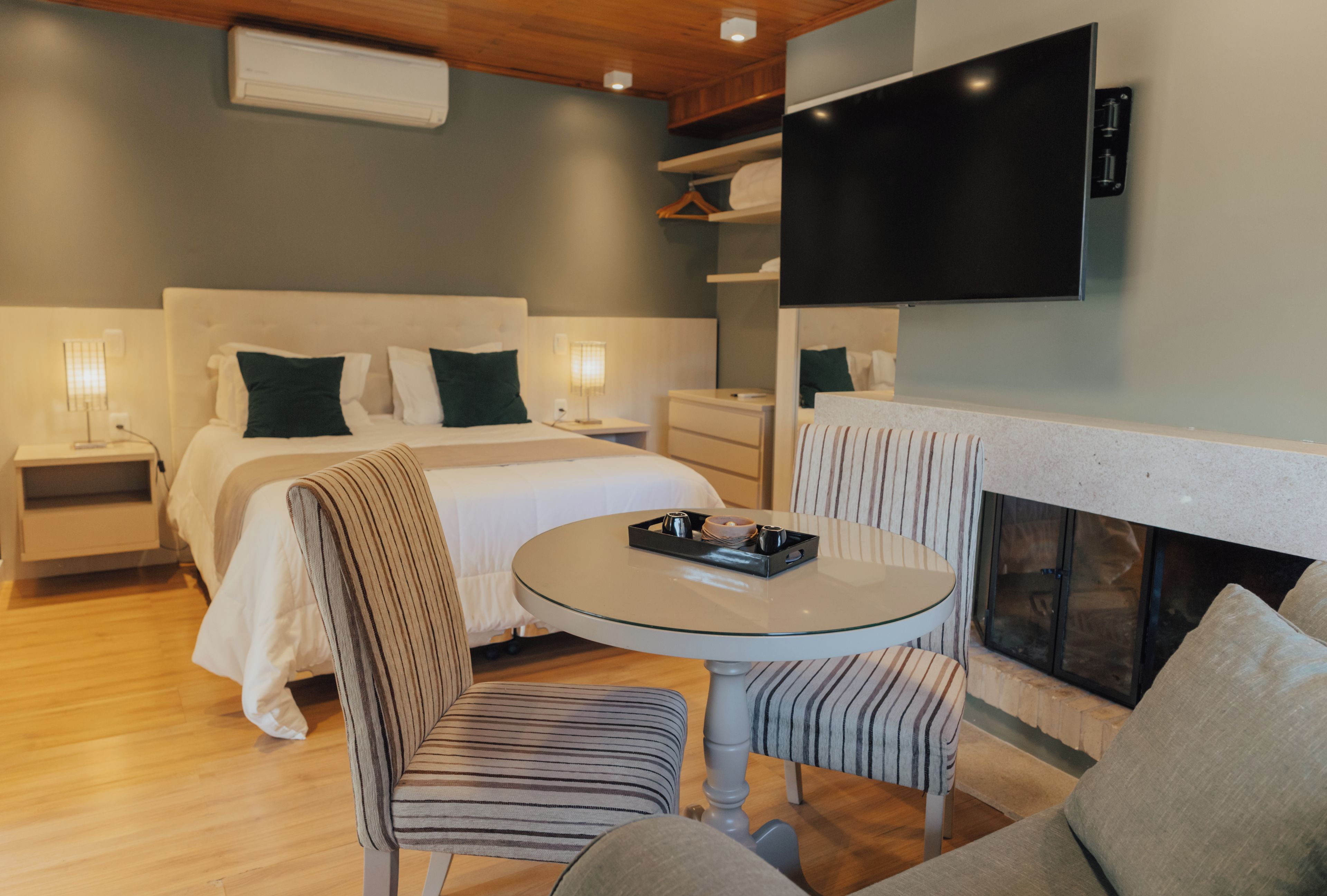 Une chambre d’hôtel moderne équipée d’un lit, de tables de chevet, d’un téléviseur à écran plat, d’une cheminée et d’une table ronde avec des chaises.