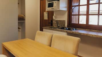 A small kitchenette with a microwave, a sink, and a window with blinds.