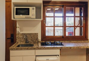 A kitchen with a built-in microwave, a gas stove, a sink, and a window with a view of the outside. - Belo Destino (Gramado)