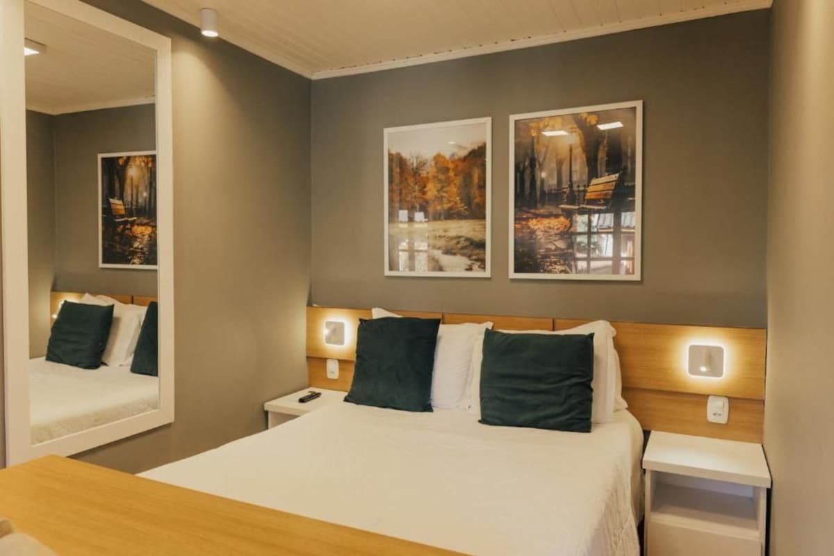 Quarto de hotel com uma cama, mesas de cabeceira, um espelho e duas quadros pendurados na parede.