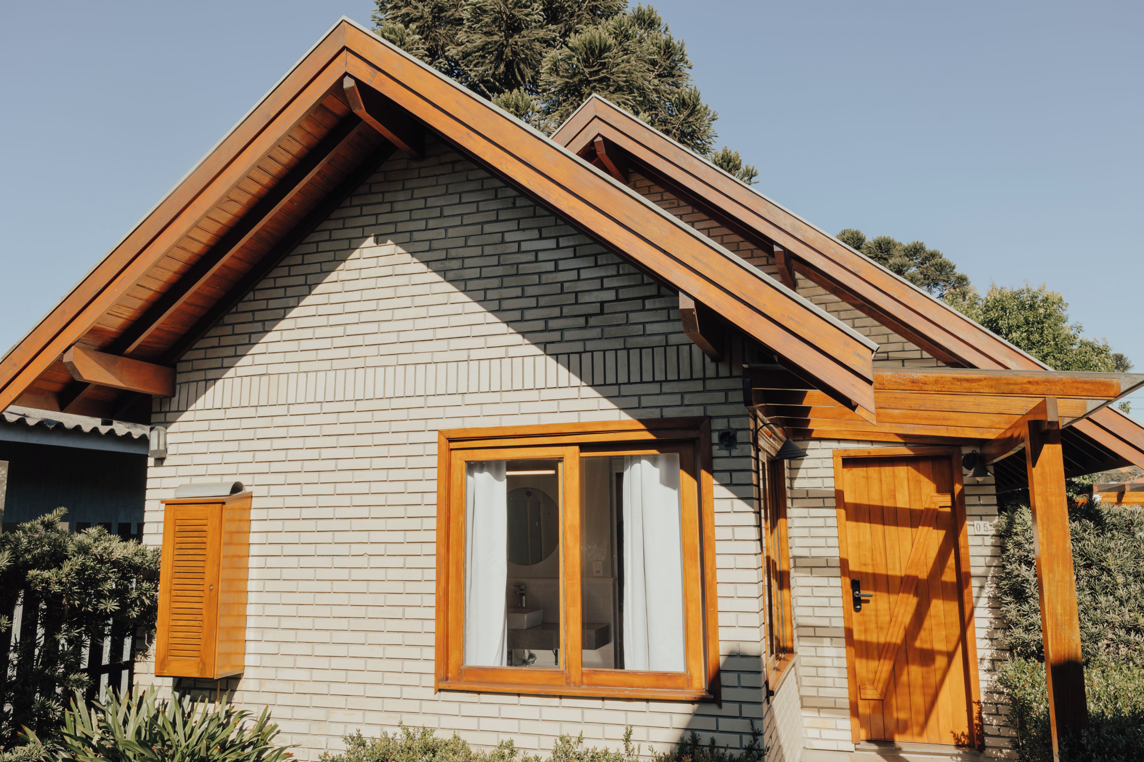 A two-story house with a pitched roof, a visible window with shutters, and a brick exterior.