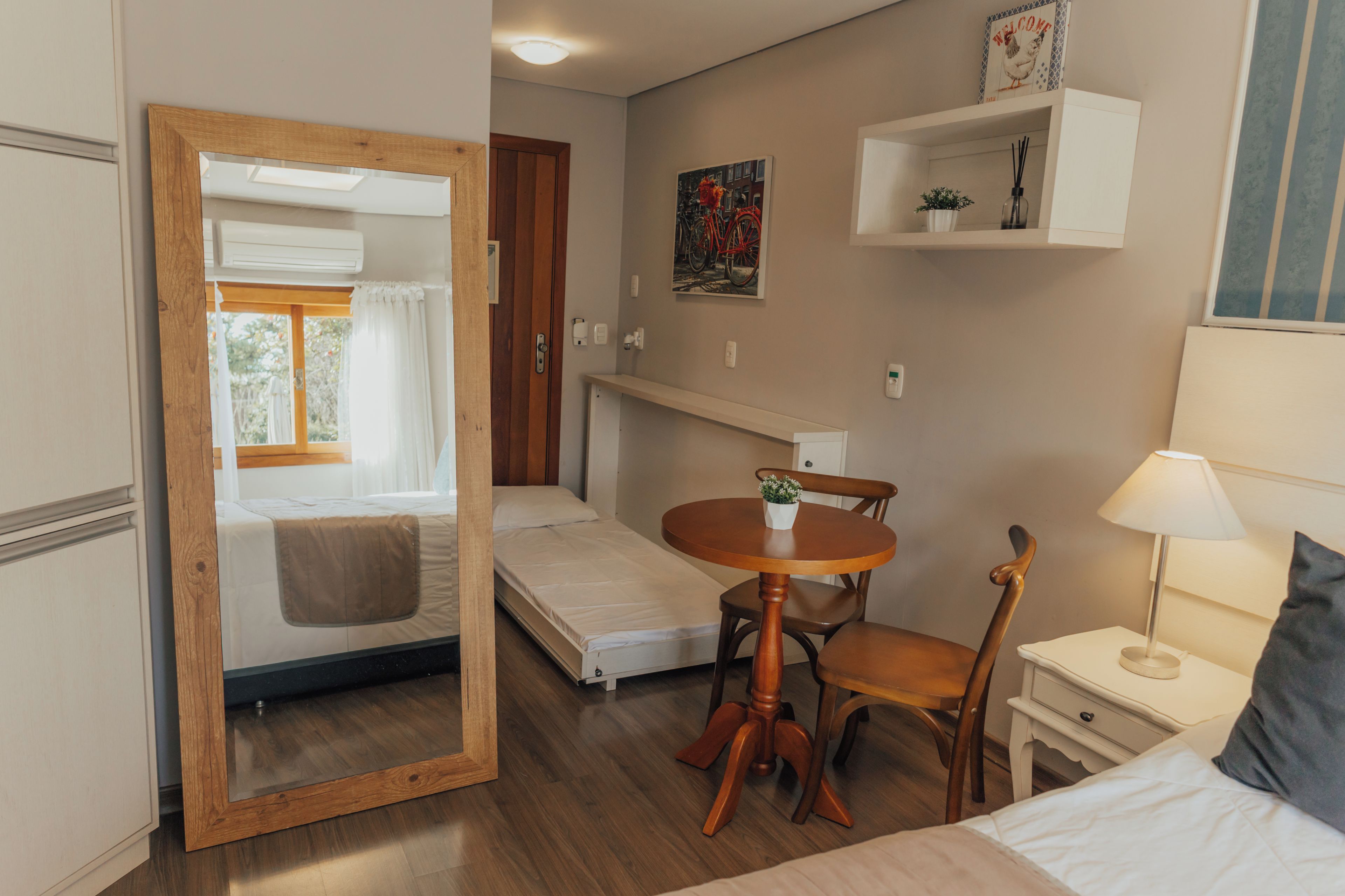 A compact room with a bed, a small table, a chair, and a mirror.