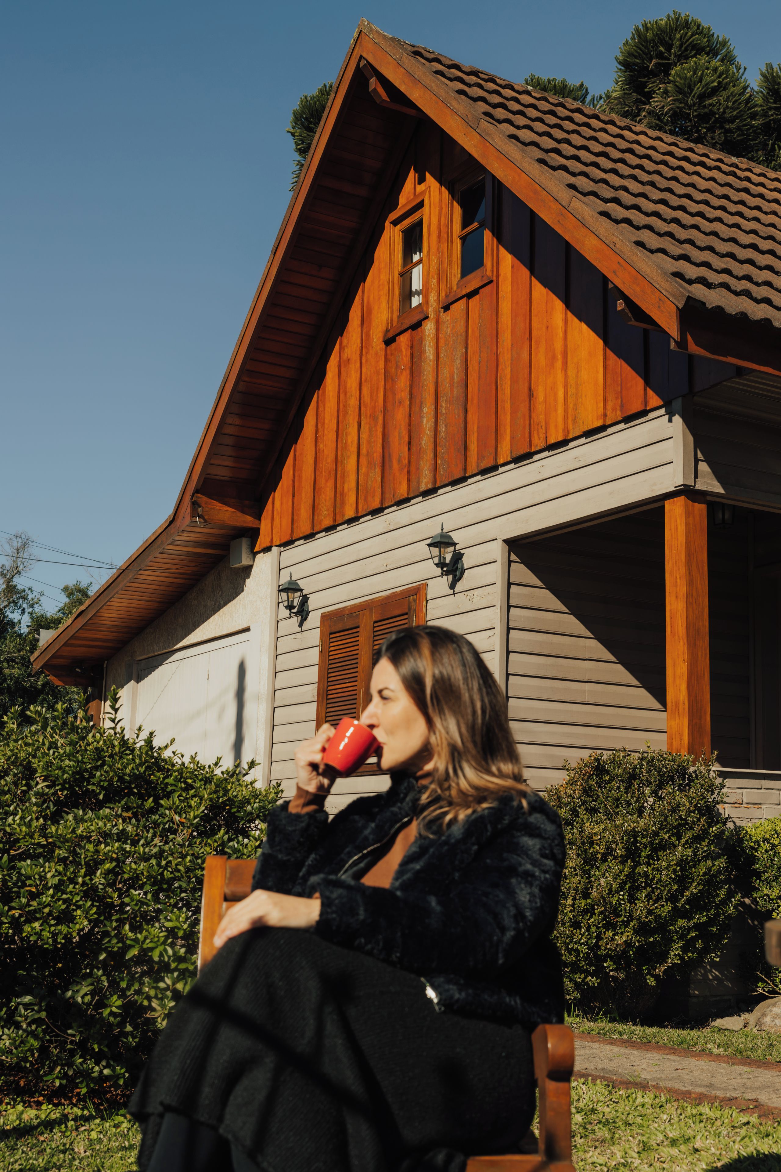 A person sitting on a bench outside a wooden house with a tiled roof.