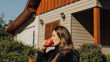 A person sitting on a bench outside a wooden house with a tiled roof.