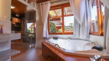 Un baño moderno con una bañera grande, una cabina de ducha con mampara de vidrio y vistas a una casa tradicional por las ventanas.