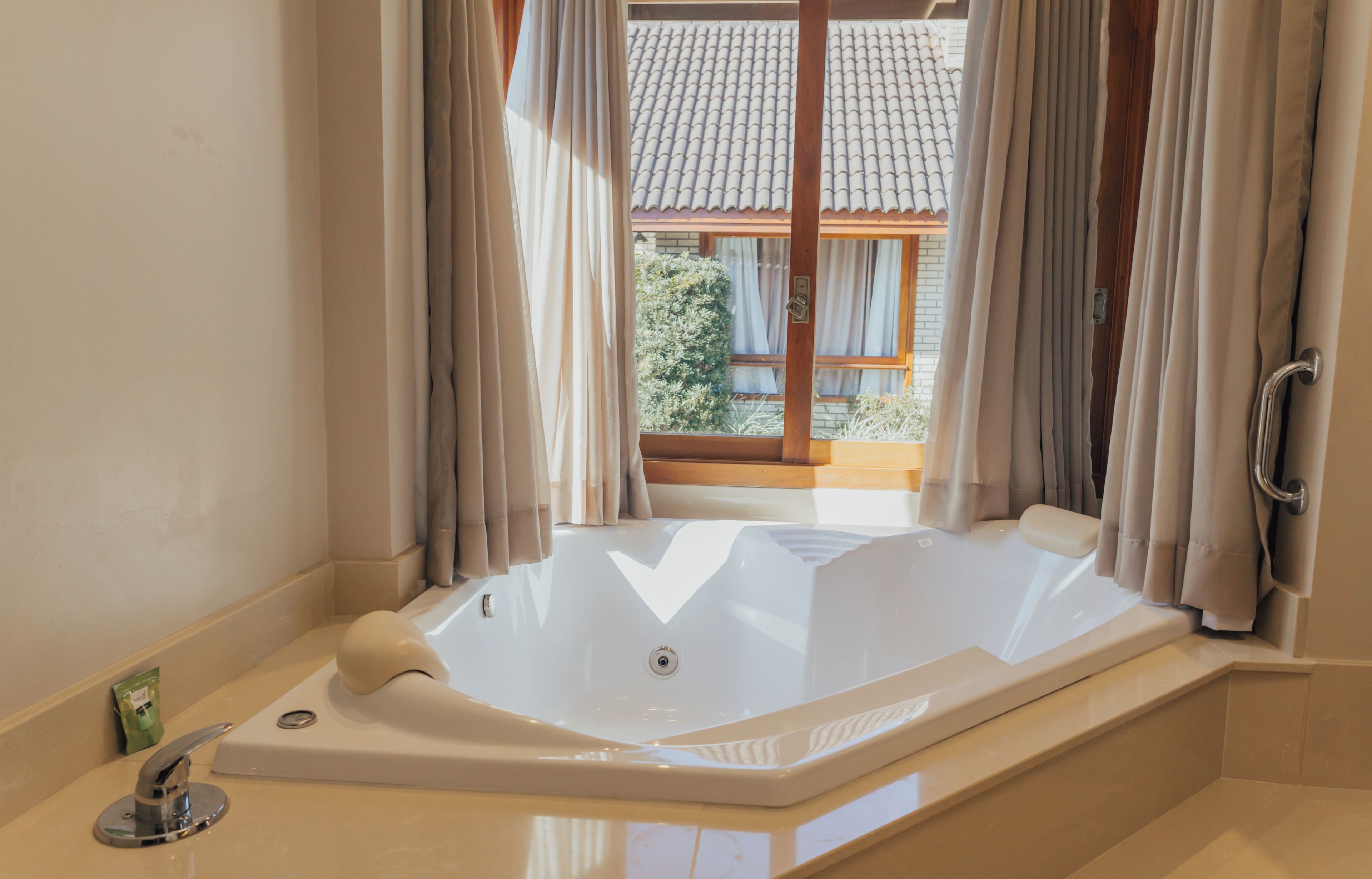 A bathroom with a large bathtub, a shower, and a window with curtains.