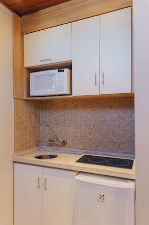 Cocina compacta con gabinetes blancos, microondas, fregadero y lavavajillas.