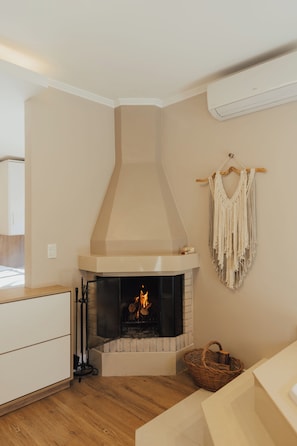 Una habitación de esquina con chimenea, un tapiz de macramé y una cesta de mimbre.