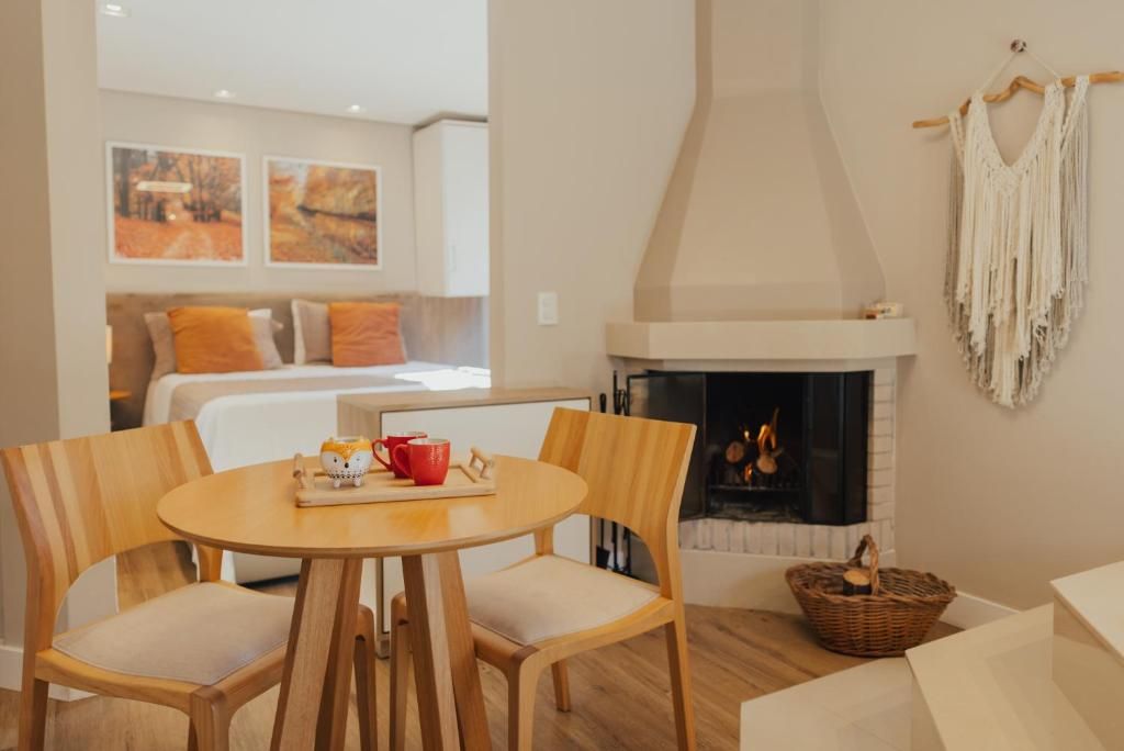 Une pièce chaleureuse avec une cheminée, un lit agrémenté d’oreillers orange, une table à manger avec des chaises et un mur décoré de tableaux encadrés.