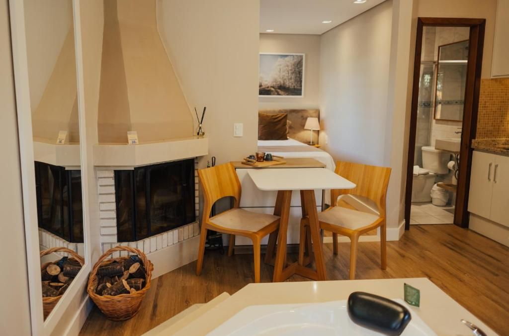 Habitación de hotel con chimenea, cama, una mesita con sillas, baño visible a través de una puerta abierta y vistas al exterior.