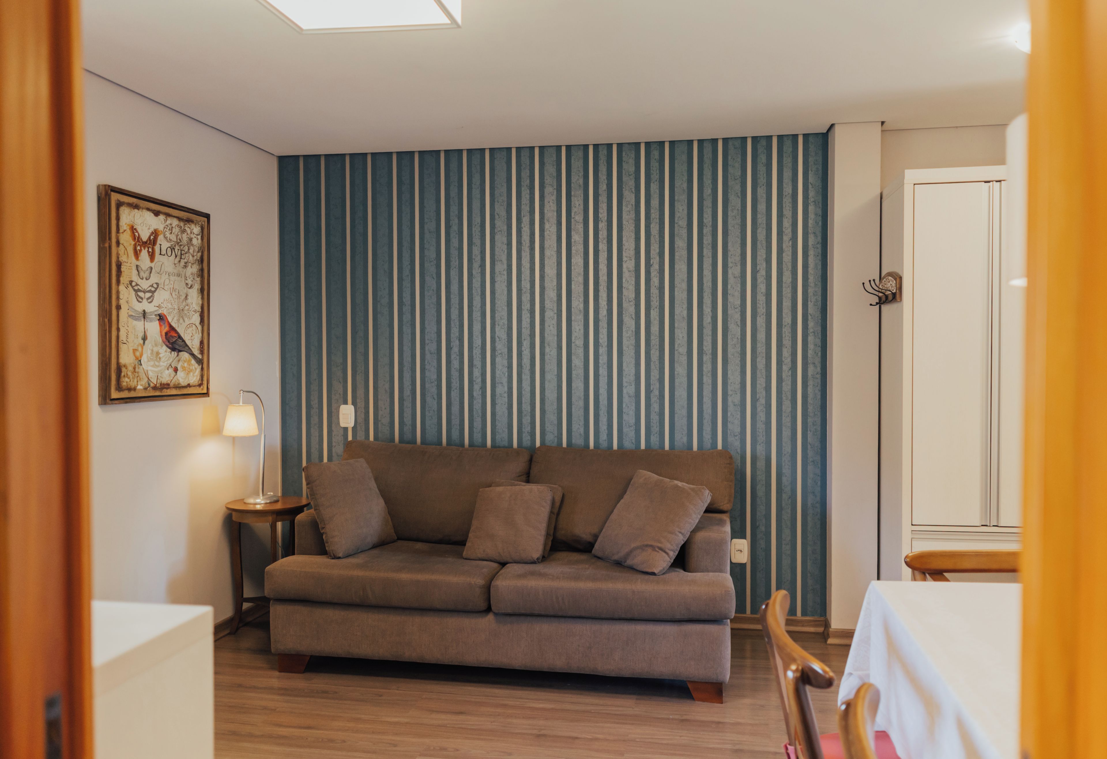 A living room with a sofa, a lamp, and a wall with vertical stripes.