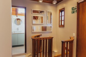 Un pasillo con barandas de madera, un espejo y un letrero que indica el camino al baño.