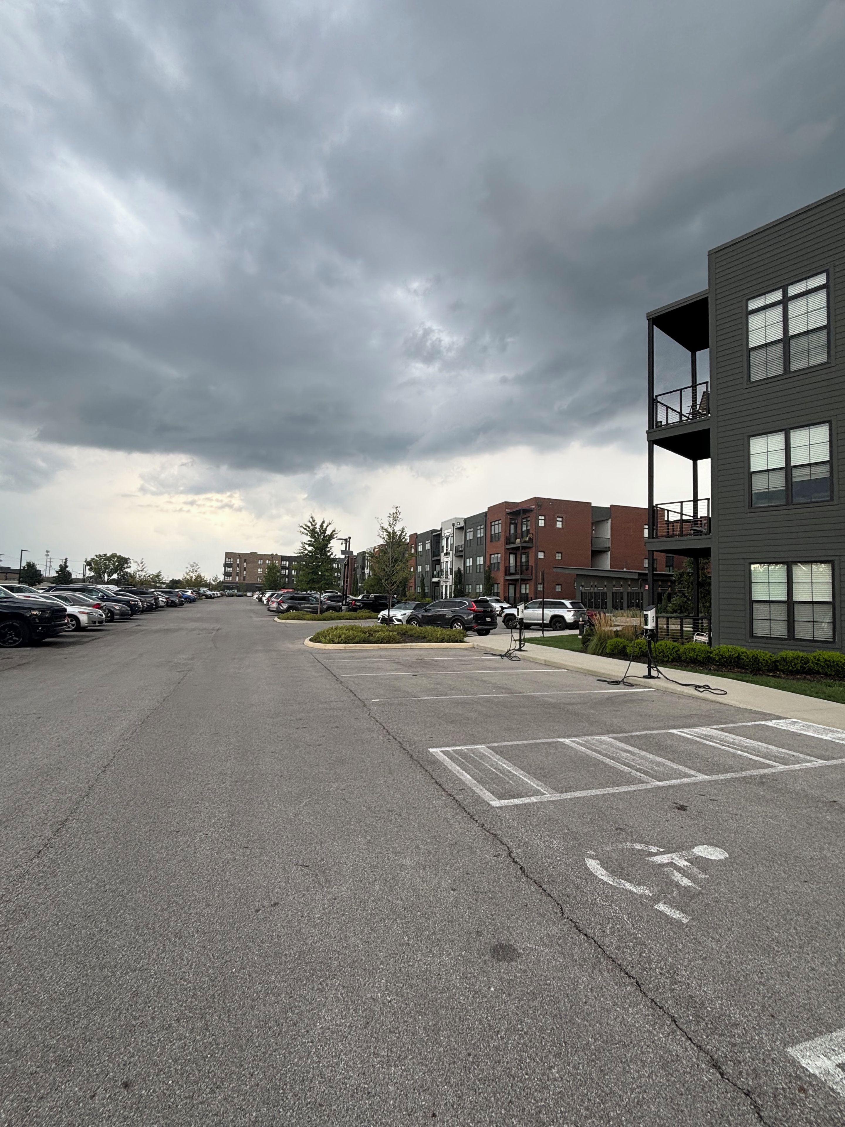 A parking lot with multiple cars, a building with balconies, and a cloudy sky.