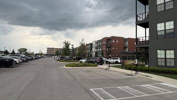 A parking lot with multiple cars, a building with balconies, and a cloudy sky.