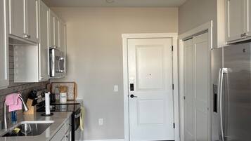 A modern kitchen with stainless steel appliances, a white door, and a dark wooden floor.