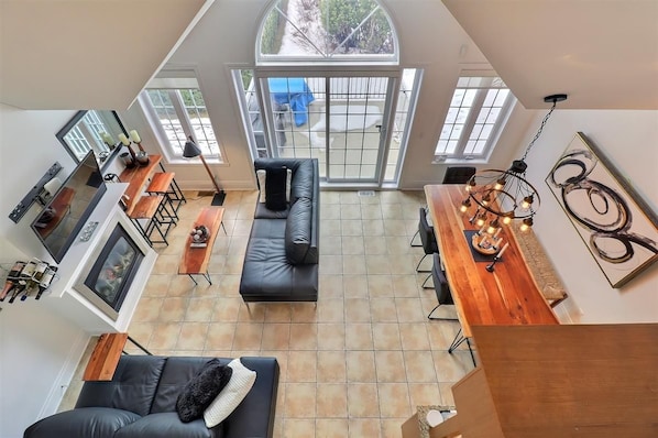 A spacious living area with a black leather sofa, wooden coffee table, and a dining table with hanging lights.