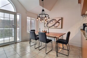 A dining area with a wooden table, four chairs, a chandelier, and a large window with a view.