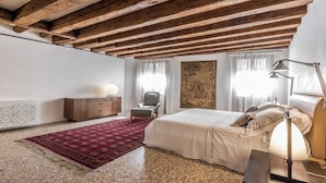 Une chambre à coucher avec un grand lit, un bureau, une chaise, un radiateur et un mur orné d’un grand tableau.