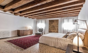 Quarto com cama grande, escrivaninha, cadeira, radiador e parede decorada com uma pintura grande.