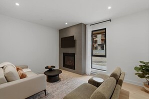 A modern living room with a fireplace, a sofa, a coffee table, and a large window with a view of a building outside. - THE VALO Ostrya 3BDR Mont-Tremblant (Mont-Tremblant)
