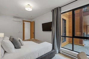 A modern hotel room with a large bed, a flat-screen TV, and a view of the outdoor area through a large window. - THE VALO Ostrya 3BDR Mont-Tremblant (Mont-Tremblant)