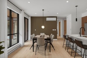 A modern kitchen with a central island, a dining area with a table and chairs, and a large window providing natural light. - THE VALO Ostrya 3BDR Mont-Tremblant (Mont-Tremblant)