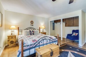 Quarto com cama, mesas de cabeceira, penteadeira, poltrona azul e guarda-roupa.