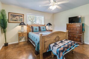 Un dormitorio con cama de madera, mesita de noche, cómoda, televisor y ventilador de techo.