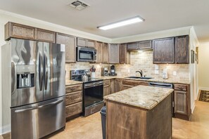 A modern kitchen with stainless steel appliances, wooden cabinets, and a granite countertop. - New 3 BDRM Lake house Mins to the Lake! (Kingsland)