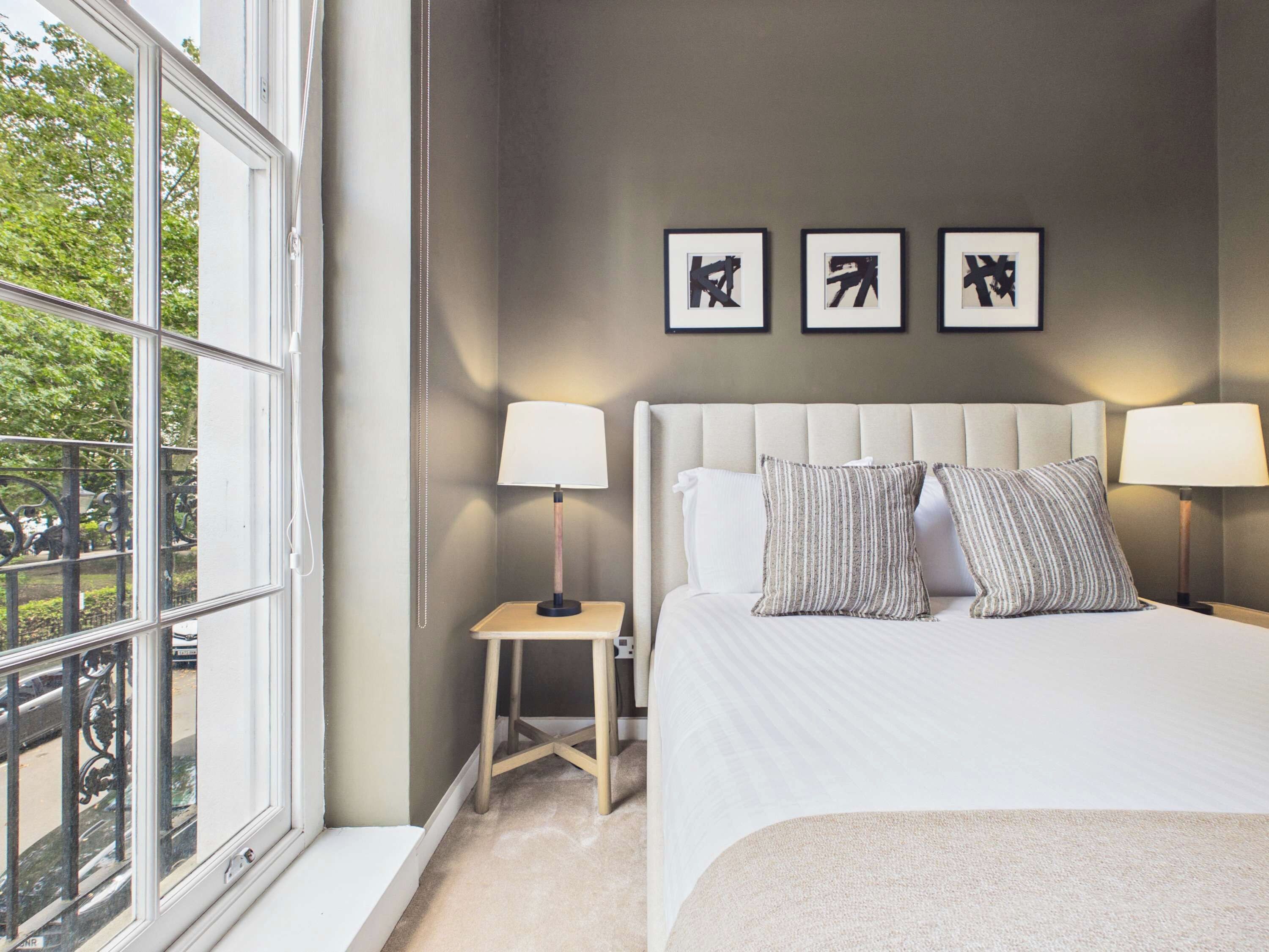 A hotel room with a large bed, two bedside lamps, a small nightstand, and three framed pictures on the wall.
